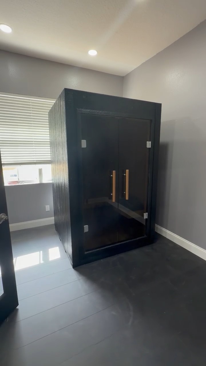 Black-clad indoor sauna with full-height glass double doors and light-wood bar handles in a grey-walled, tiled room